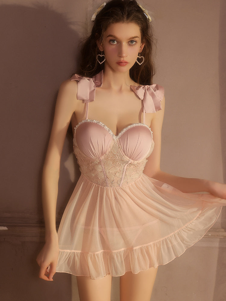 Woman wearing a pink lace pink babydoll dress with bow straps against a neutral background