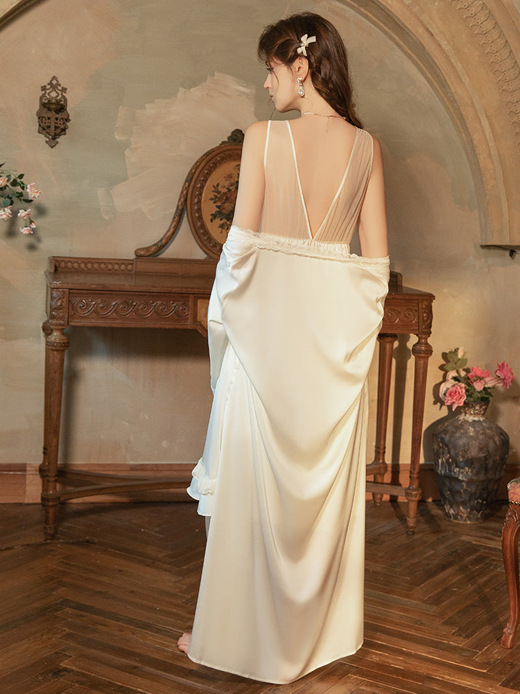 Woman in a flowing white dress standing in an elegant room with wooden floor and decorative wall.