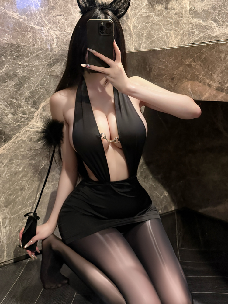 Person wearing a Plunge Halter Ring Detail Black Mini Dress Bodysuit and sheer stockings, sitting against a marble wall.