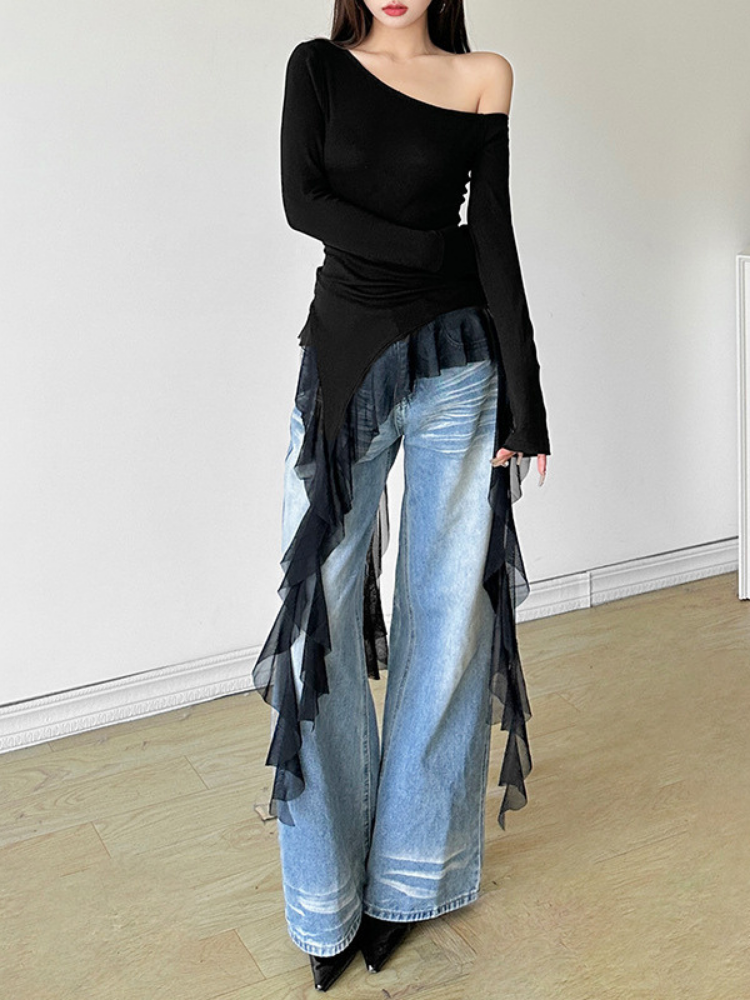 Person wearing a black off-shoulder top and light blue jeans with ruffled details on a plain background