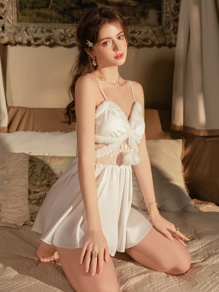 Woman in a White Satin Faux Fur Slip Dress sitting on a bed in a warm-toned room.