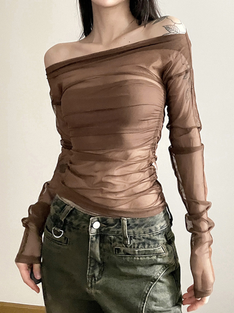 Person wearing a brown off-shoulder top with long sleeves and green pants on a plain background