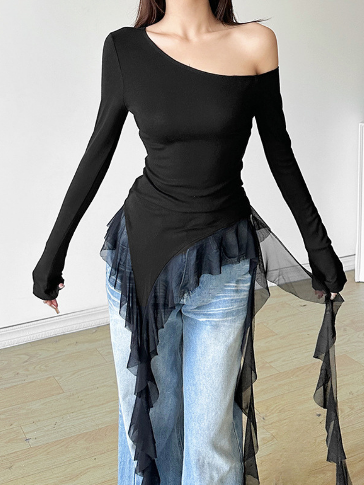 Person wearing a black off-shoulder top with sheer overlay and light blue jeans indoors.