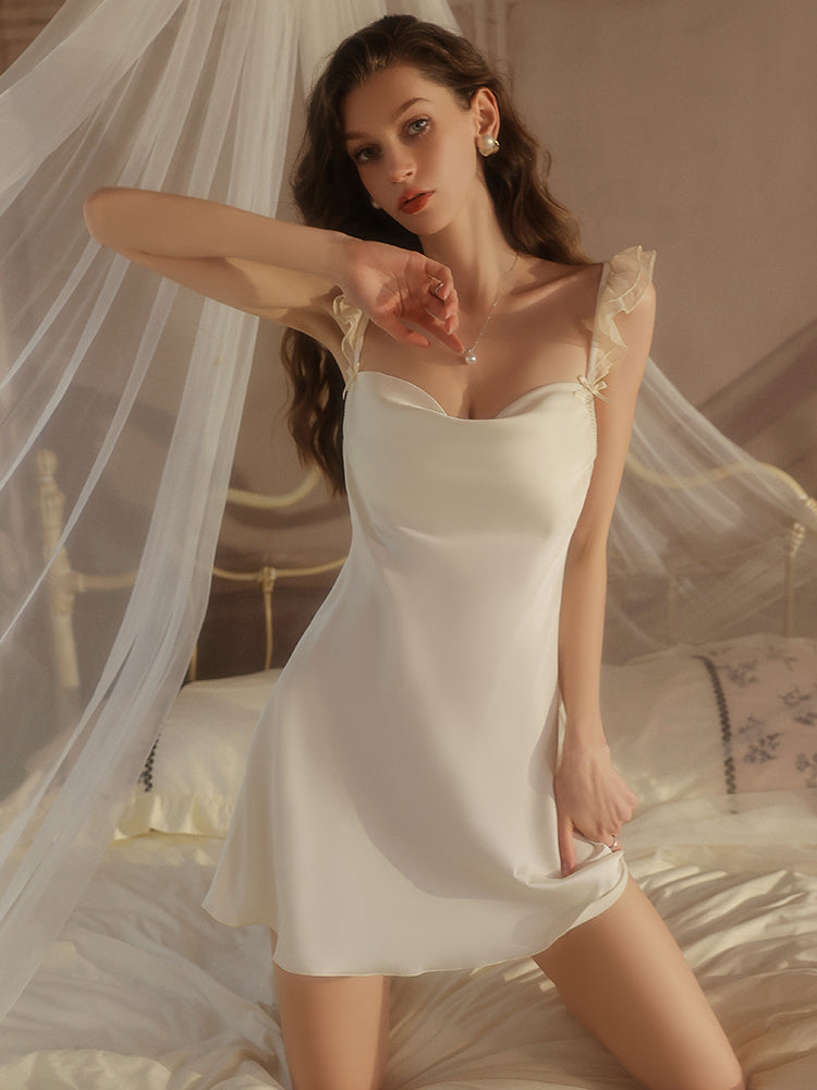Woman wearing a white satin nightgown in a softly lit bedroom setting.