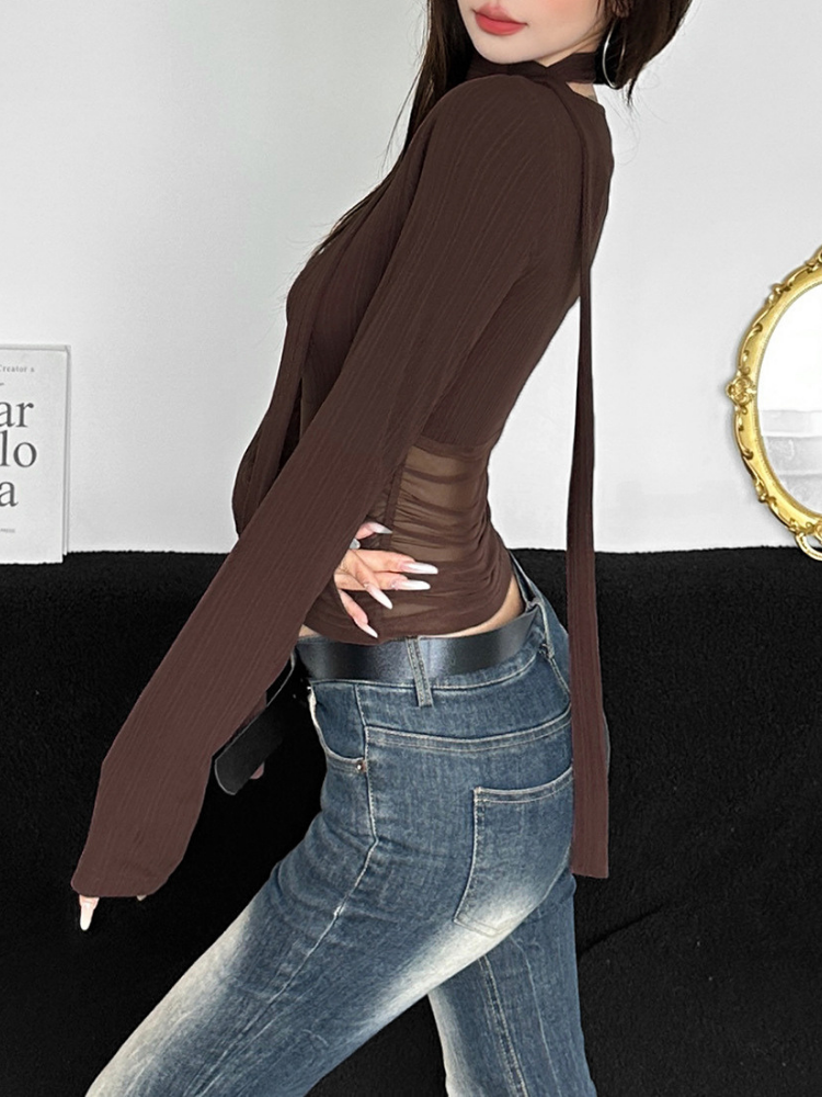 Person wearing a brown long-sleeve top and blue jeans against a white wall.