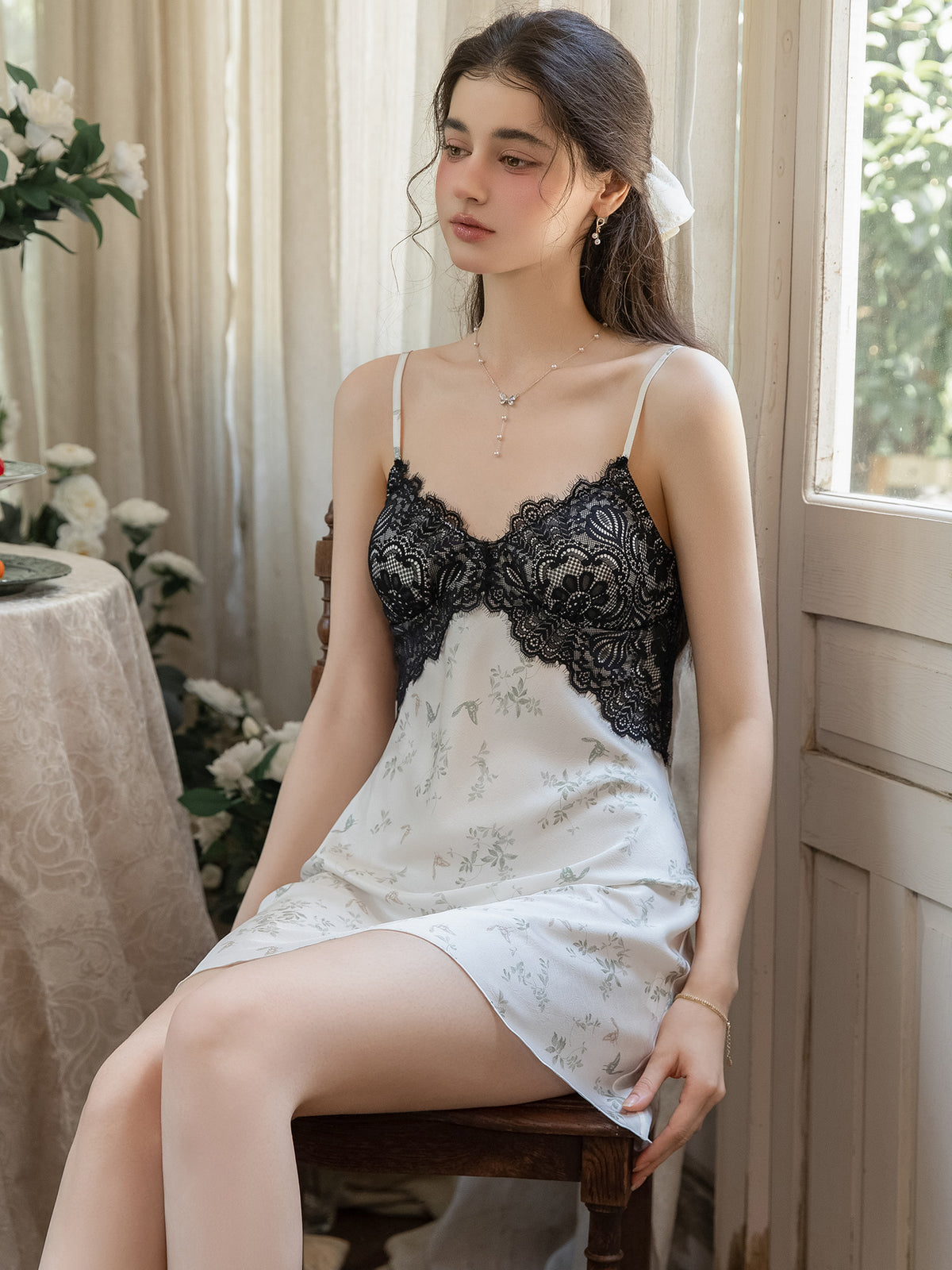 Seated front view of white floral print nightgown and black lace neckline