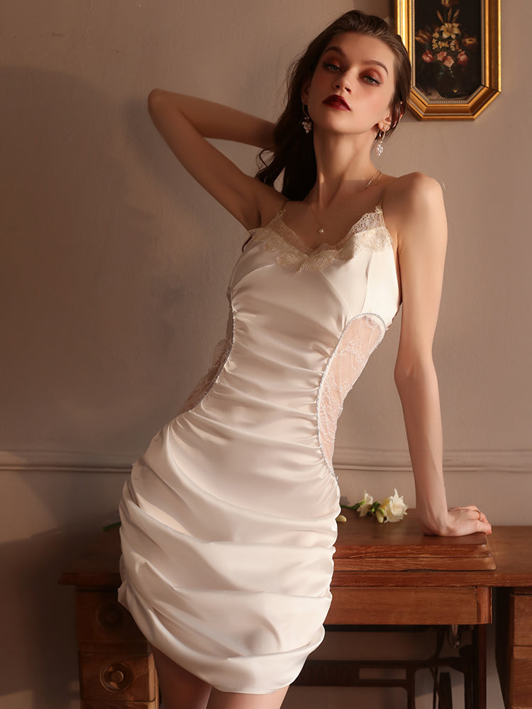 Woman in a cream satin slip dress with lace detailing, leaning against a vintage dresser under warm light, creating a timeless aesthetic.