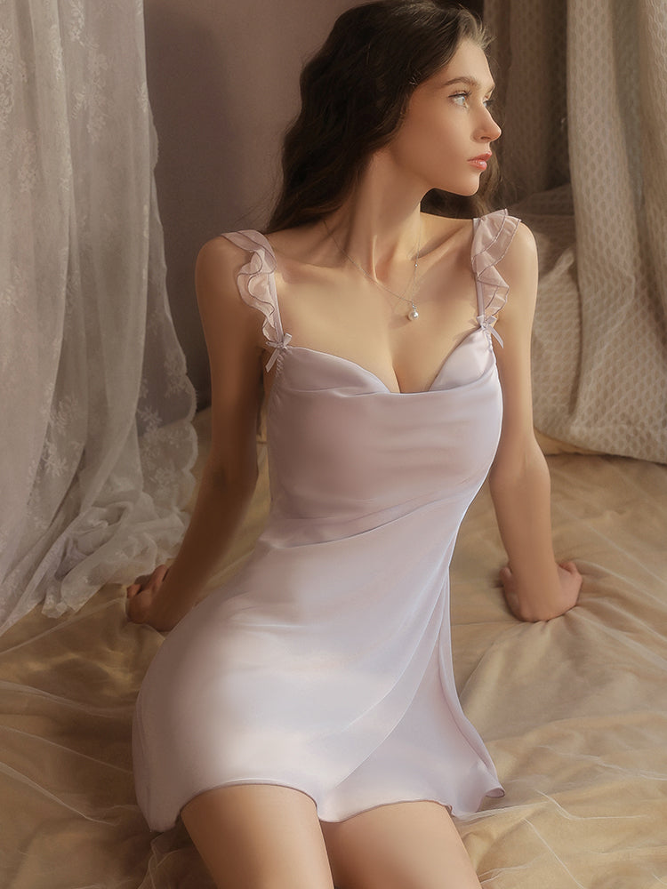Woman in a white satin nightgown sitting on a bed with curtains in the background