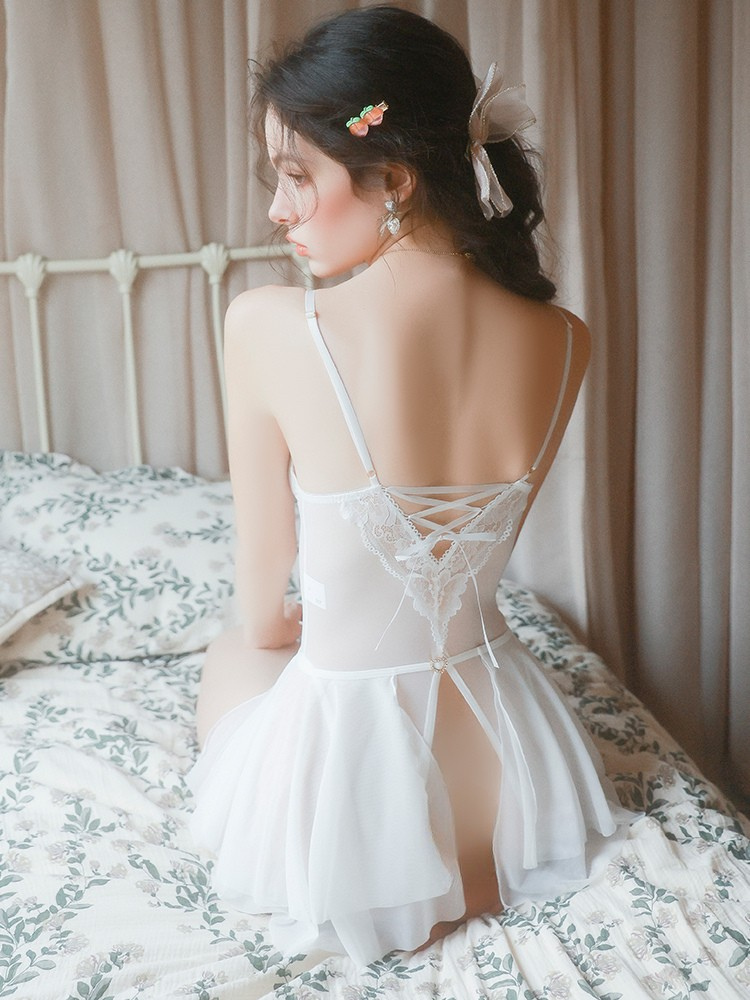 Woman in a white lace dress sitting on a bed with floral patterns.