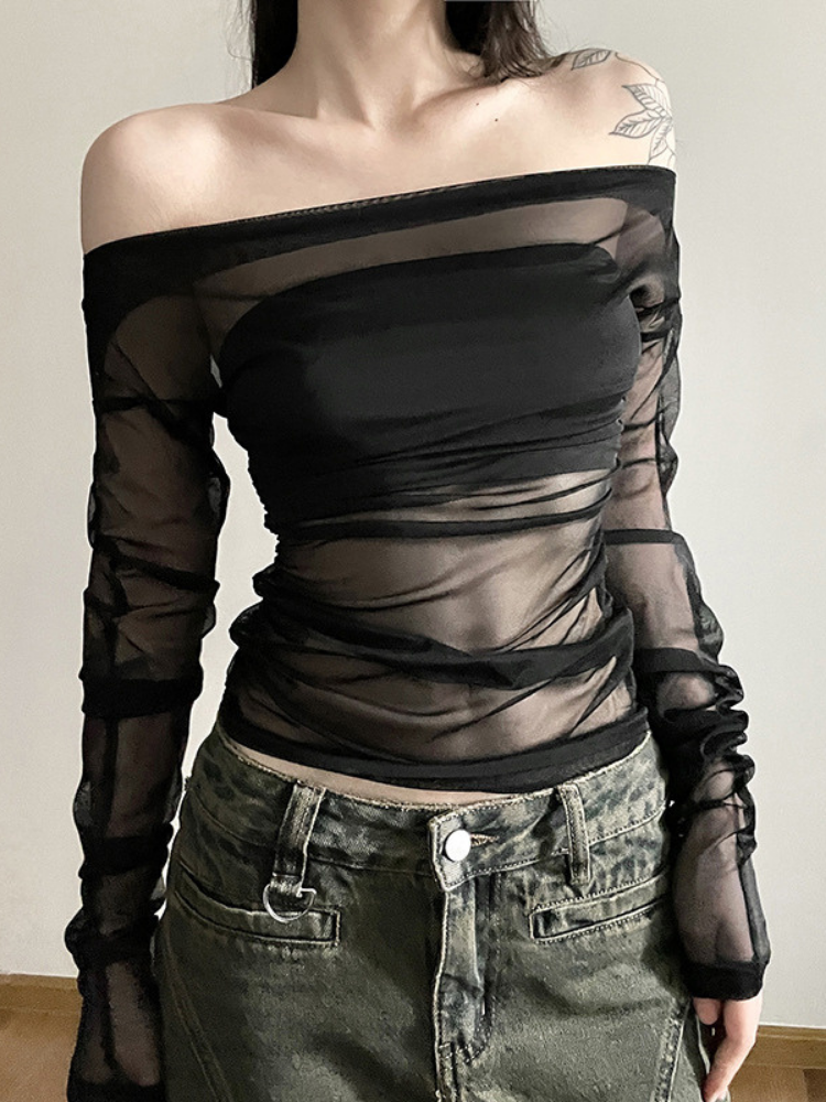 Person wearing a sheer black top and green pants against a neutral background