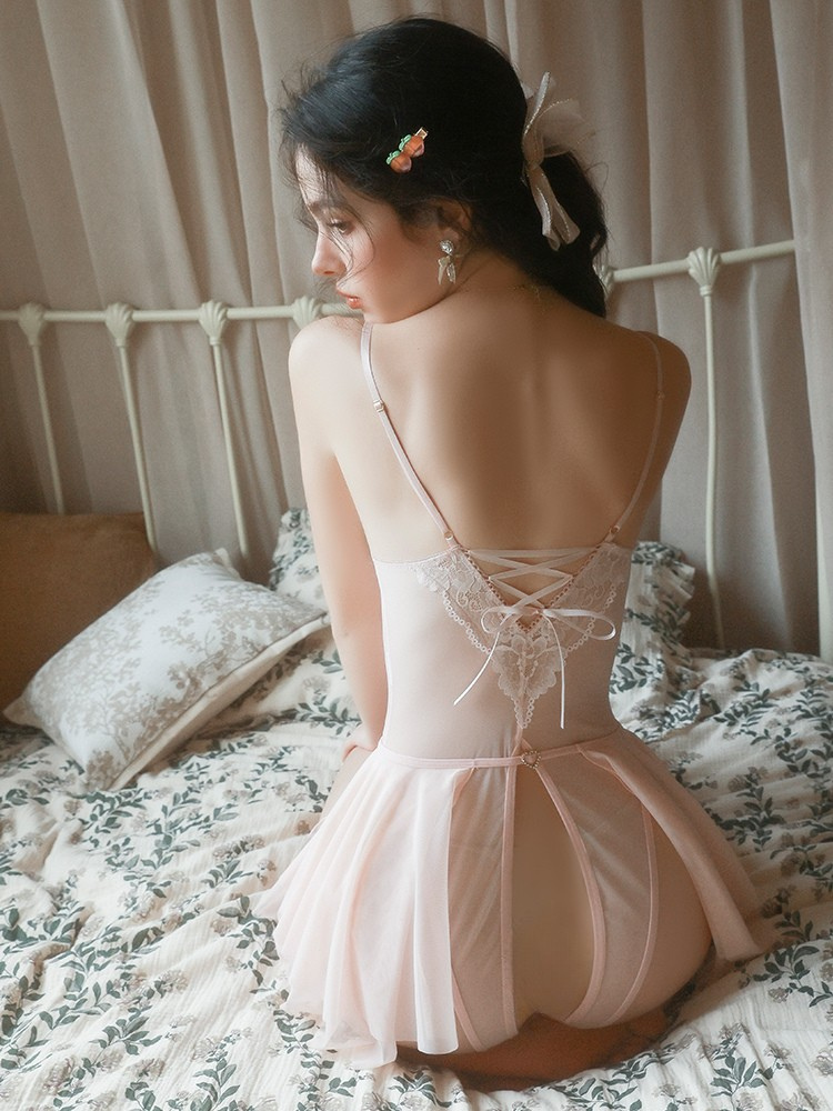 Woman in a delicate pink dress sitting on a bed with floral patterns.