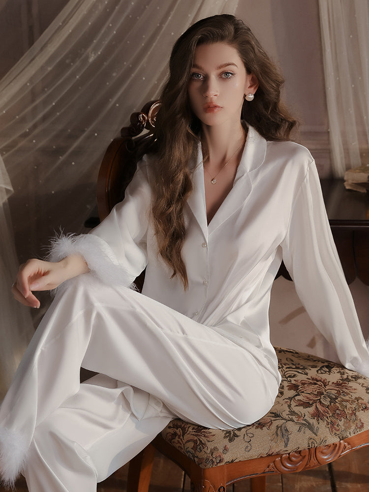 White satin pajama set with delicate feather accents on the cuffs, paired with wide leg pants for a cozy yet stylish sleepwear look.