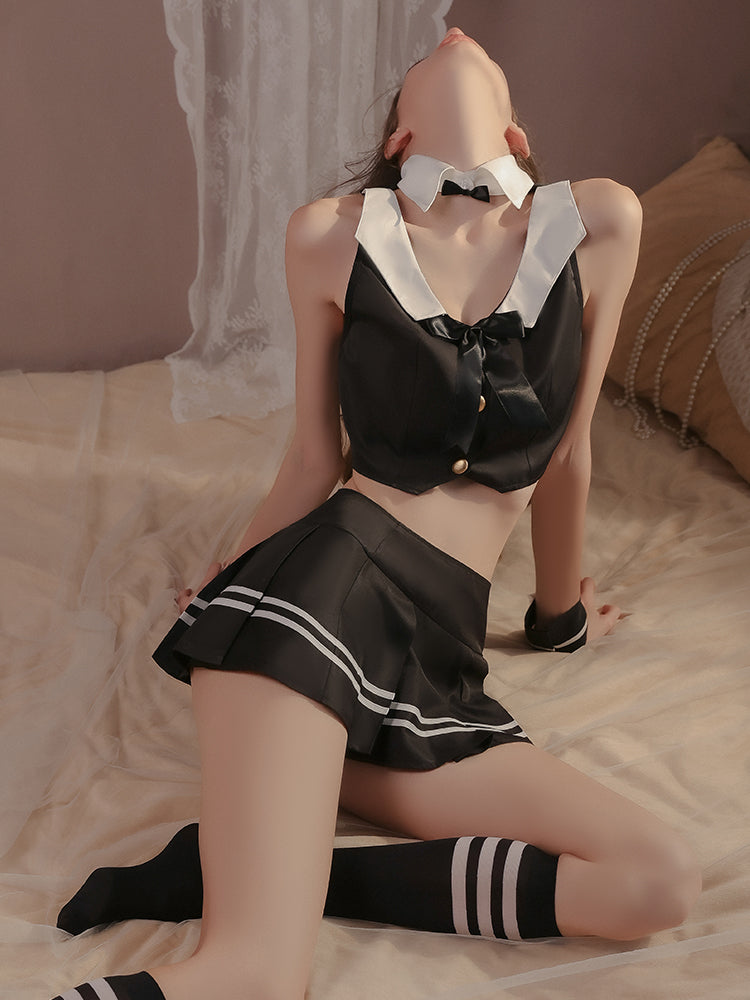 Close up of a black satin lingerie set showcasing the bow tie detail on the cropped top and pleated mini skirt with white stripe accents, styled with matching striped socks.