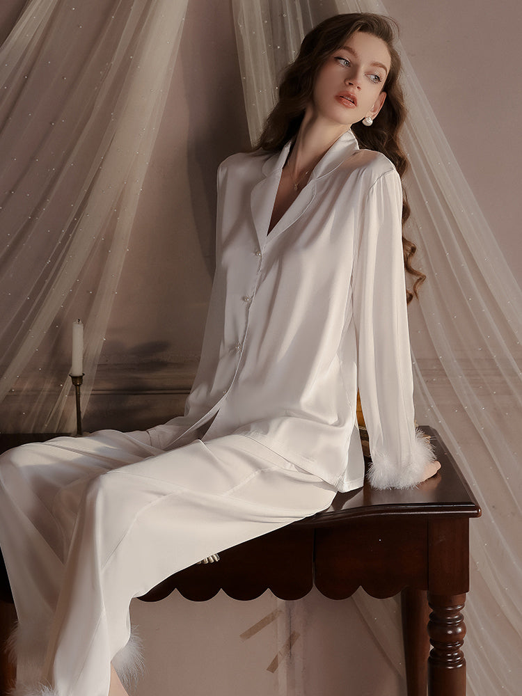 Luxurious white satin pajama set with feather detailed cuffs and a button up shirt, designed for premium lounging or sleeping.