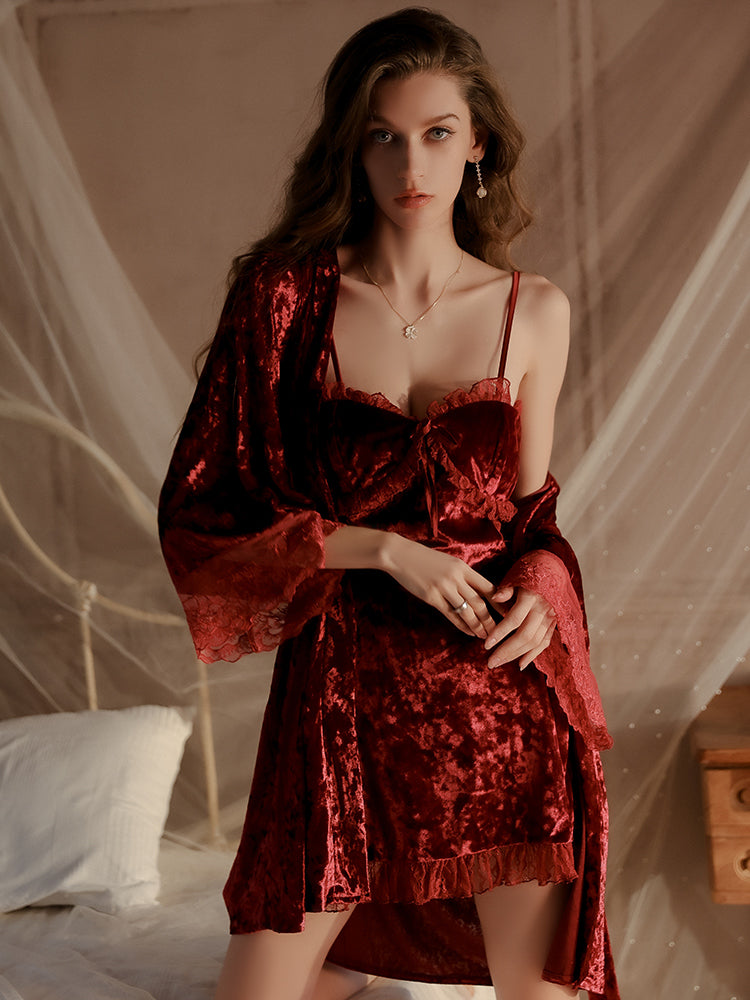 Model wearing a rich red velvet slip dress with delicate lace trim and a matching long robe, sitting gracefully on a vintage bed with a soft draped backdrop.