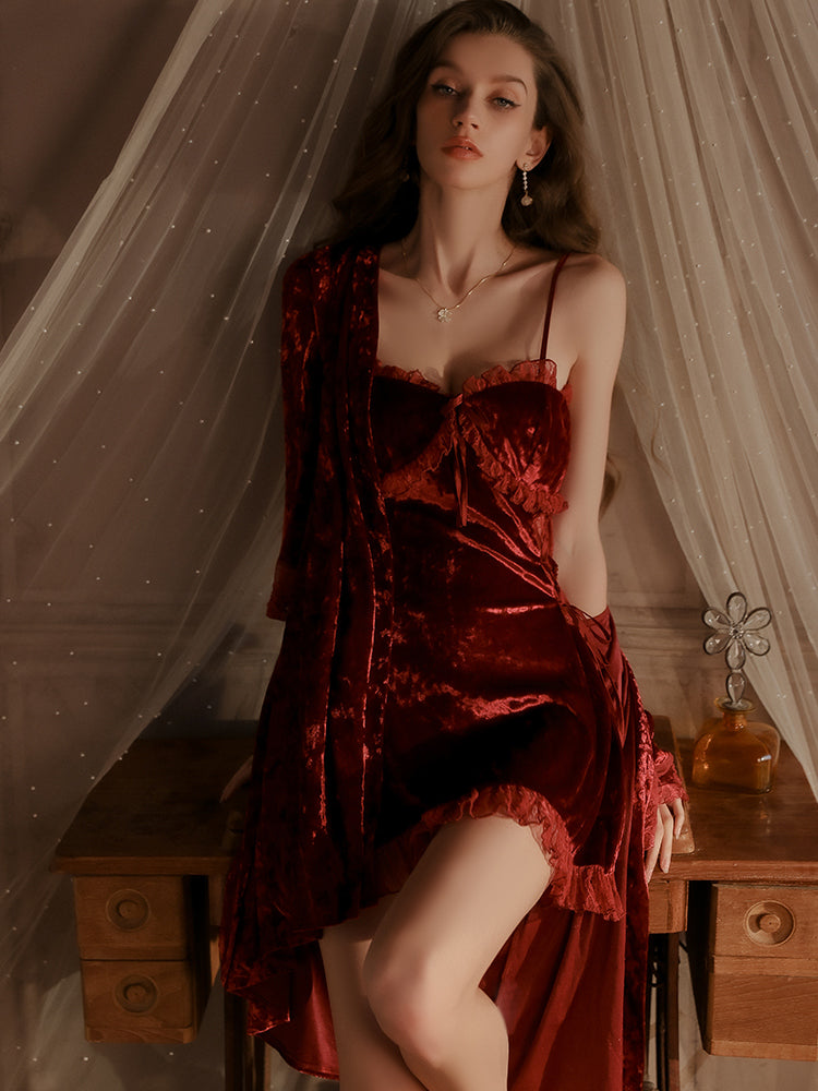 Close up of a model in a deep red velvet slip dress with intricate lace details and spaghetti straps, standing elegantly beside a wooden vanity table, exuding classic charm.