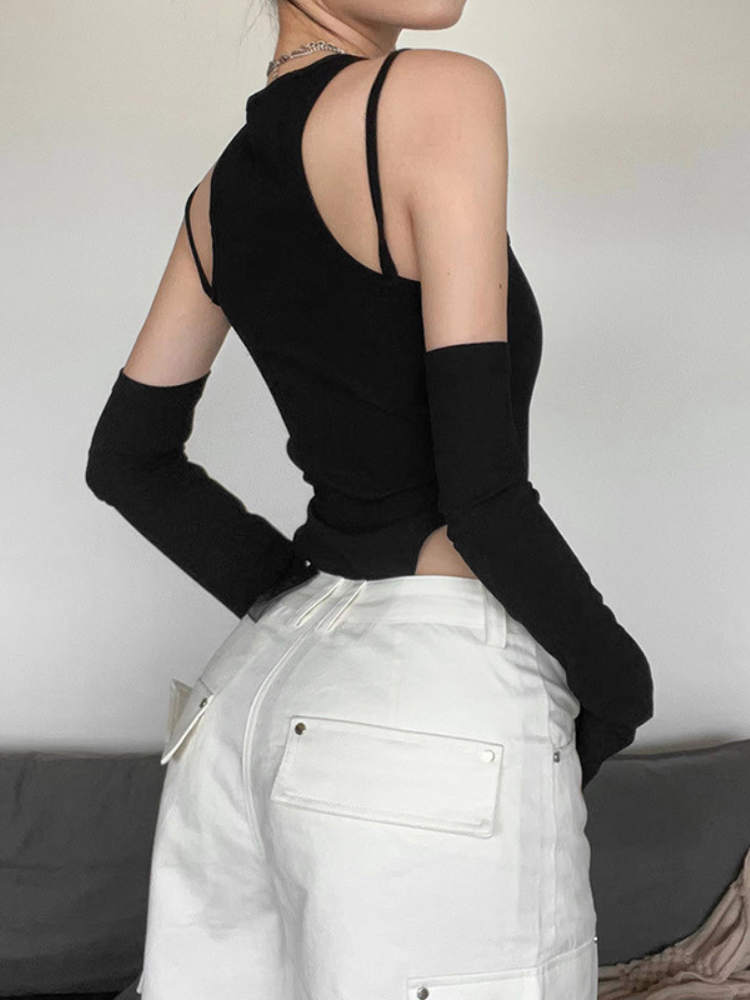 Person wearing a black sleeveless top with cut-out shoulders and white pants against a neutral background