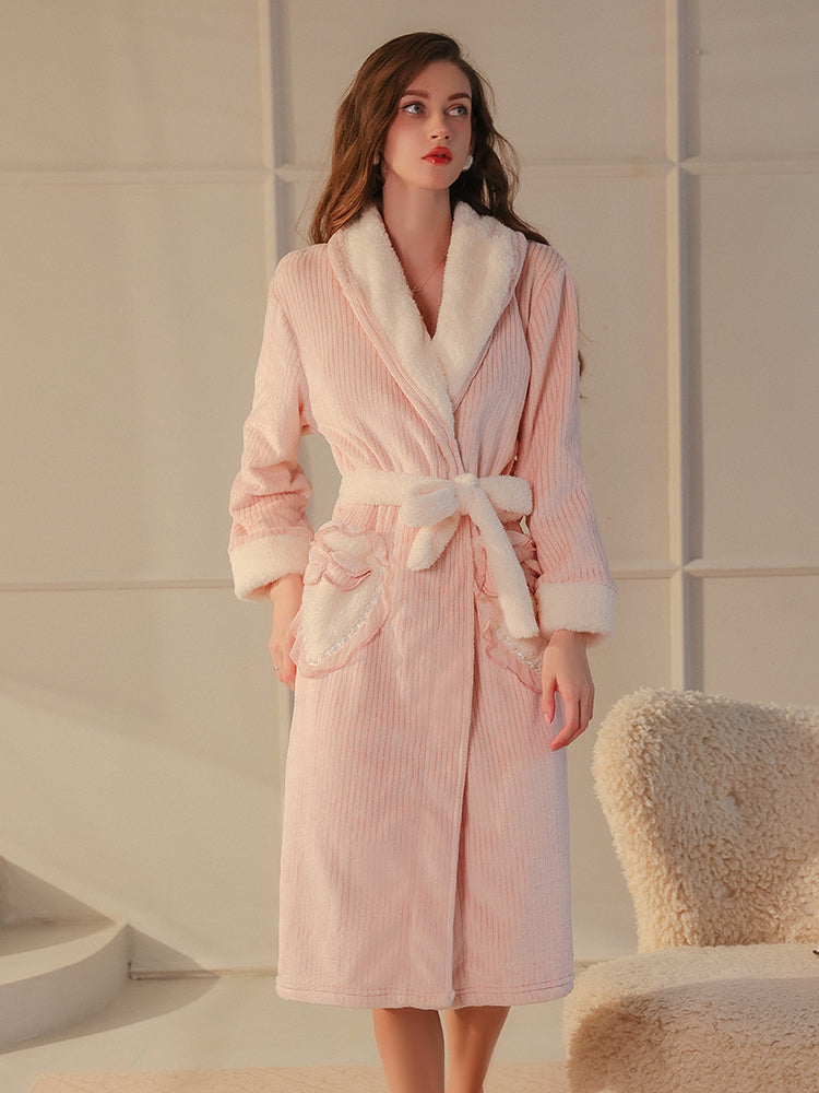 A full length pink plush textured robe with a wrap around belt and fleece cuffs, model standing in a neutral pose.