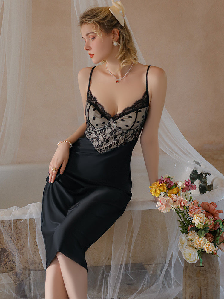 Woman in a Lace Bodice Satin Midi Slip Dress Black sitting on a couch with flowers and bottles in the background