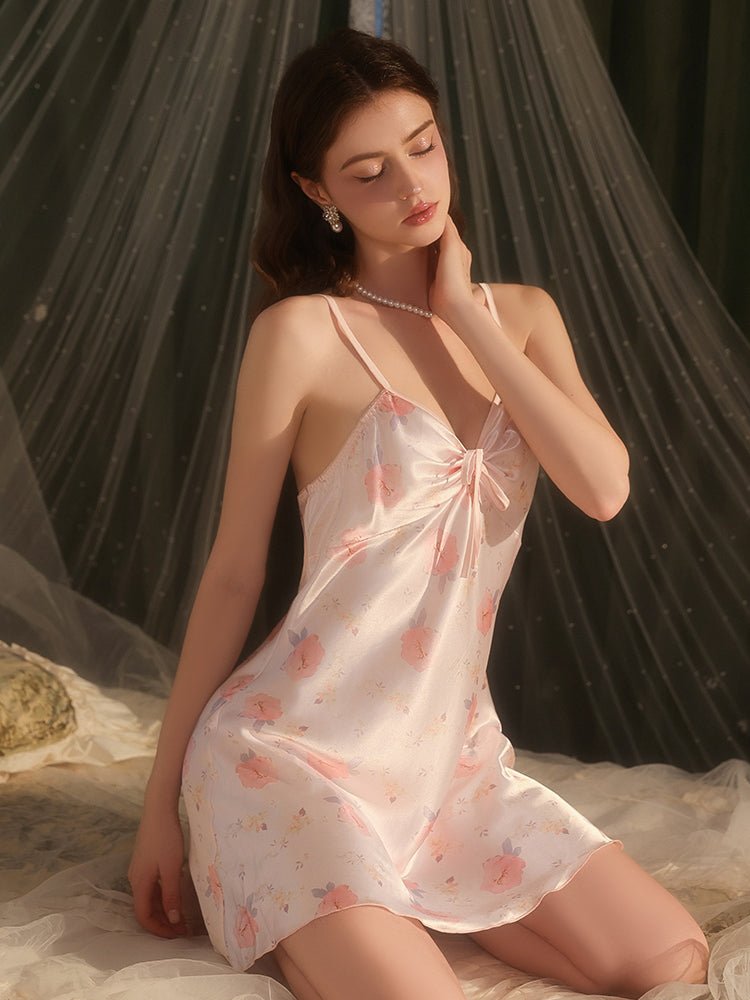 Woman wearing a floral nightgown sitting on a bed with sheer curtains in the background