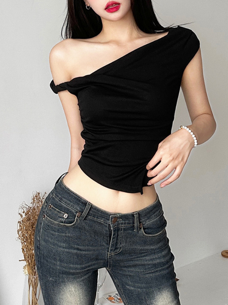 Woman wearing a black one-shoulder top and blue jeans against a plain background