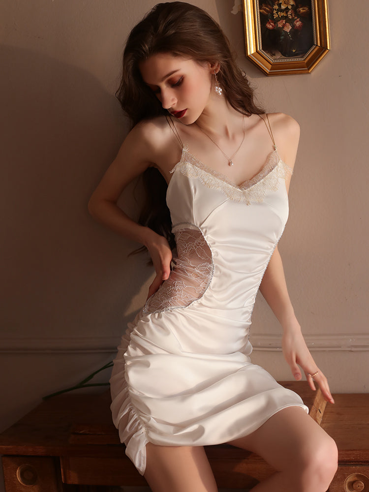 Woman in a cream satin slip dress with lace detailing, leaning against a vintage dresser under warm light, creating a timeless aesthetic.