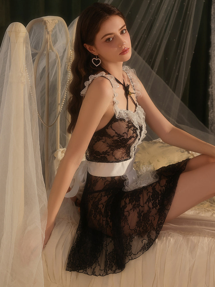 Woman in a black lace dress sitting in a softly lit room with sheer curtains.